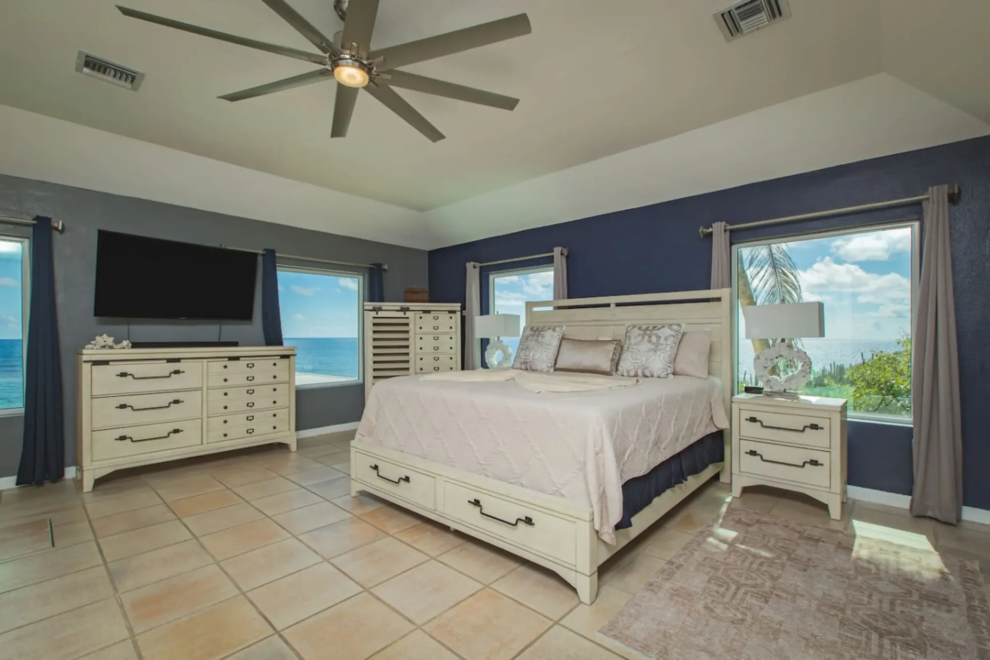 A bedroom with blue linens and an ocean view
