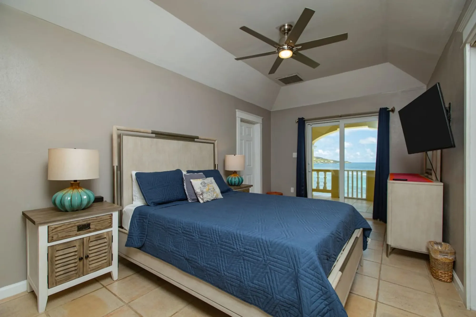 A bedroom with blue linens and an ocean view